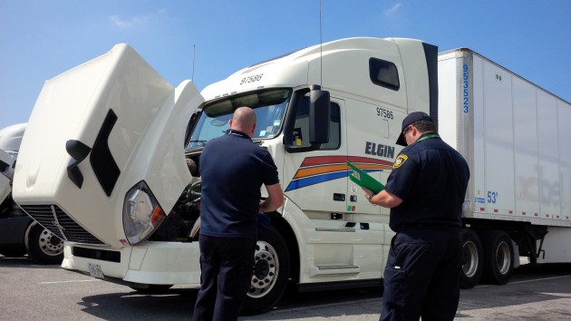 A driver completes his pre-trip as an MTO officer looks on.