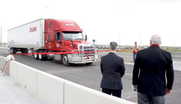 An Orlicks Inc. truck drives through the ribbon at the 61st Ave. S.E. extension opening June 23, as Gene Orlick and Mac Logan look on.
