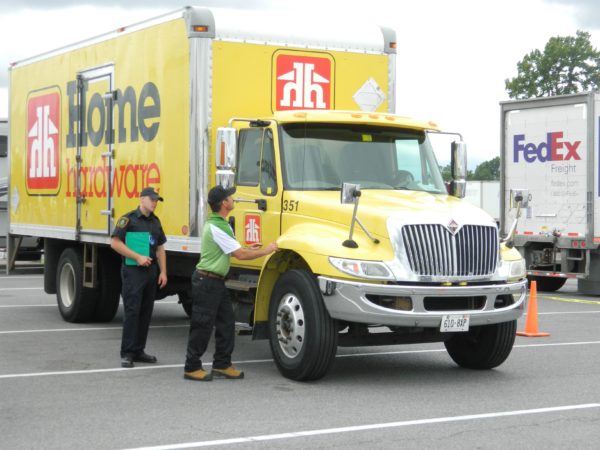 A driver does the pre-trip inspection portion of the competition as an MTO officer looks on.